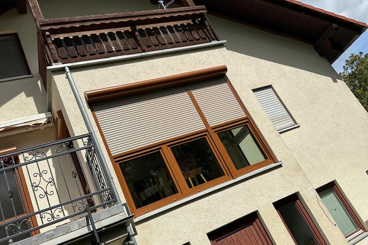 Hausfassade mit Holzbalkon und Fenstern in Holzdekor mit Rollläden