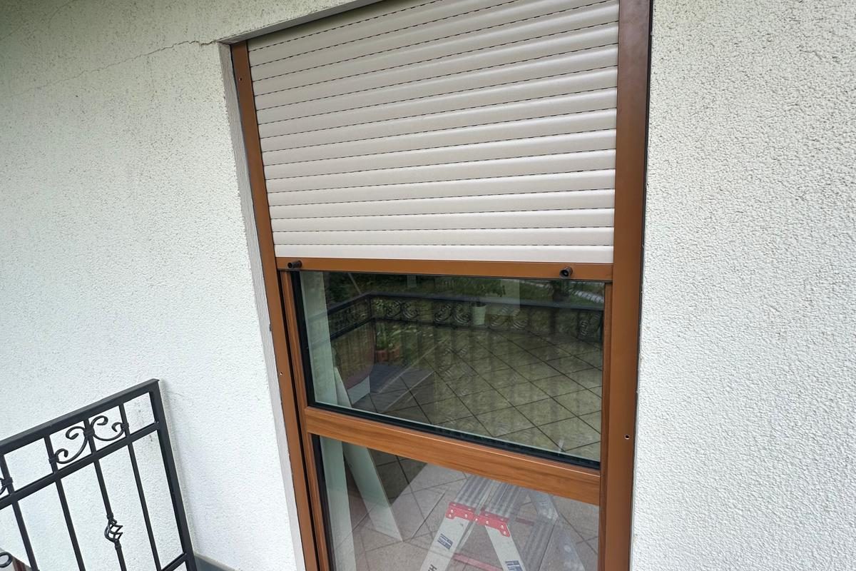 Halb geschlossener heller Rollladen vor einer Balkontür in Holzdekor