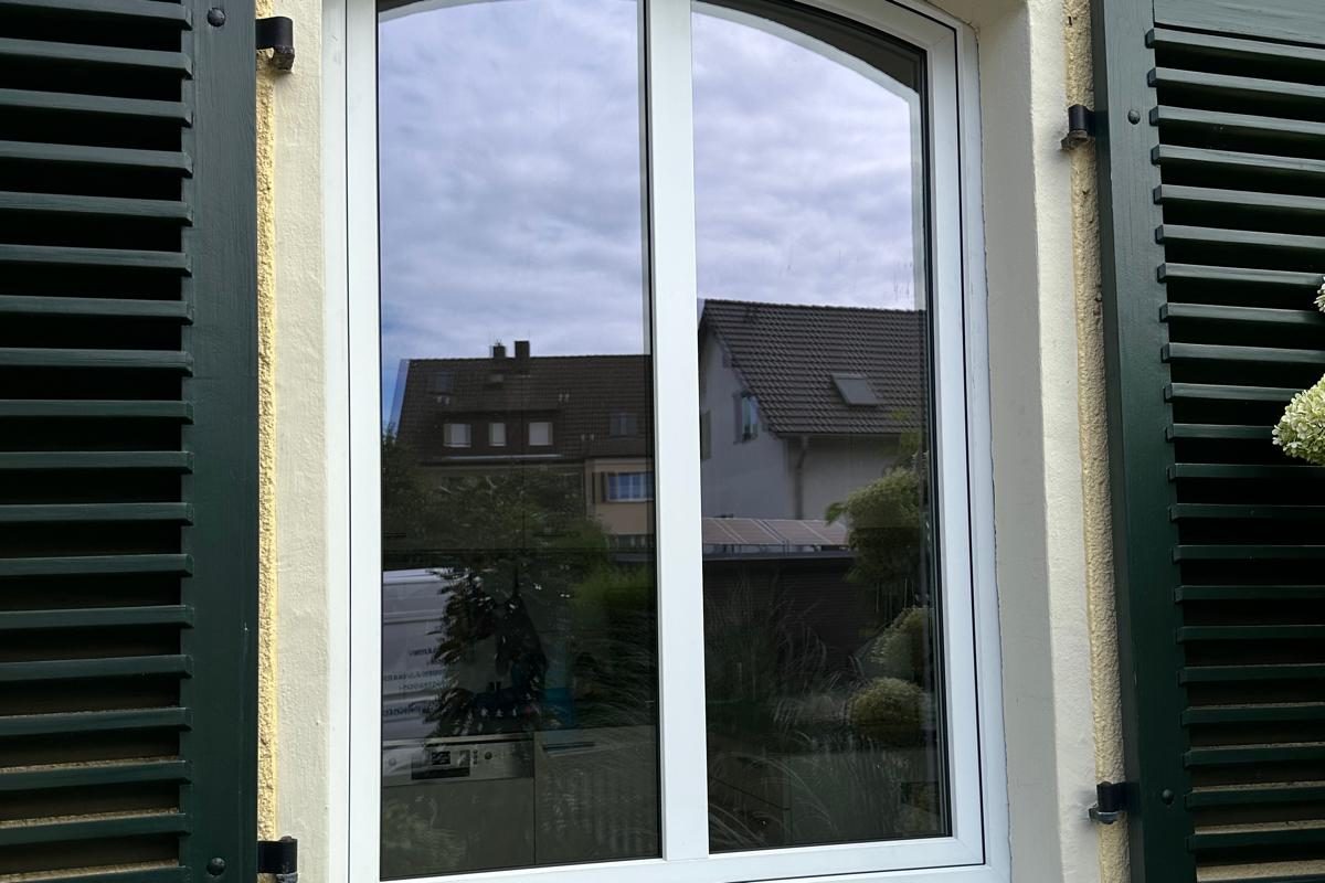 Weißes Rundbogenfenster zwischen dunkelgrünen Klappläden an einer gelben Fassade