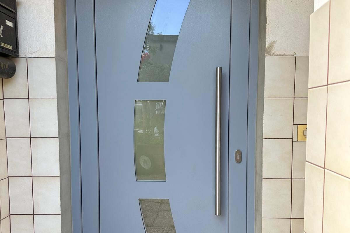 Graue Haustür mit drei geschwungenen Glaseinsätzen und Stangengriff
