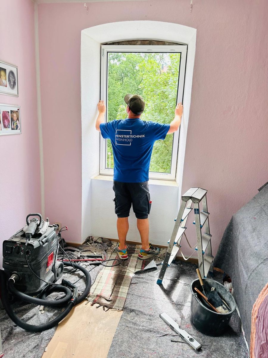 Monteur setzt ein neues Rundbogenfenster in eine frisch verputzte Fensteröffnung ein
