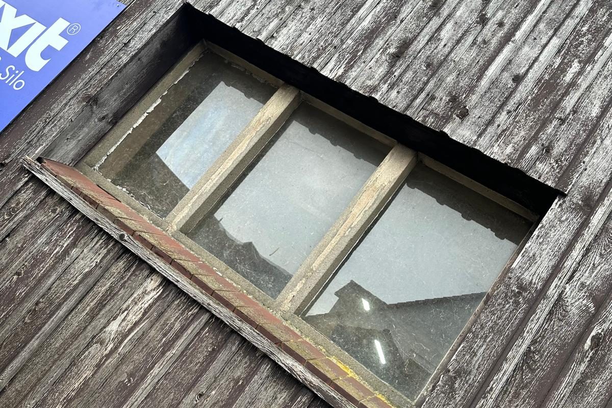 Altes, verwittertes Holzfenster mit Sprossen in einer Holzschalung
