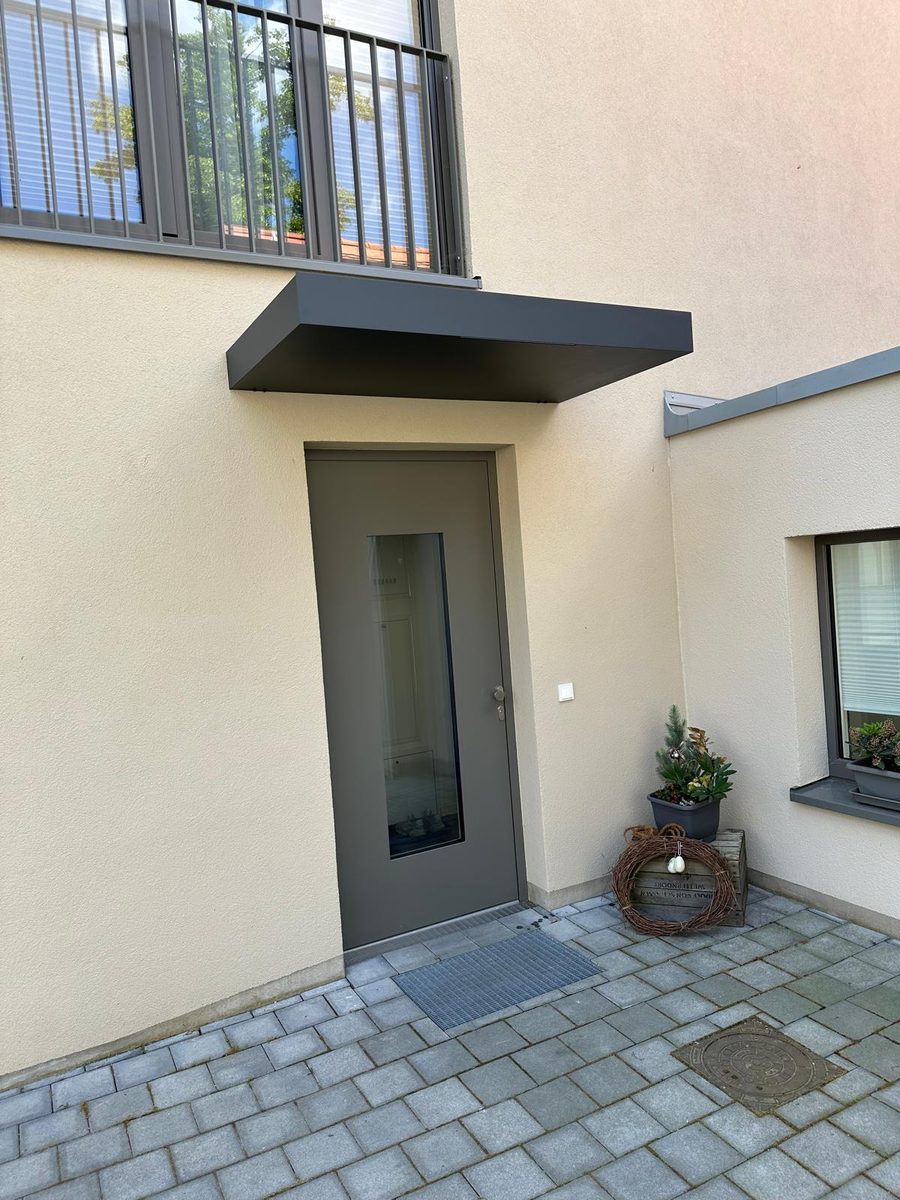 Graue Haustür mit schmalem Glasausschnitt unter einem dunklen Vordach