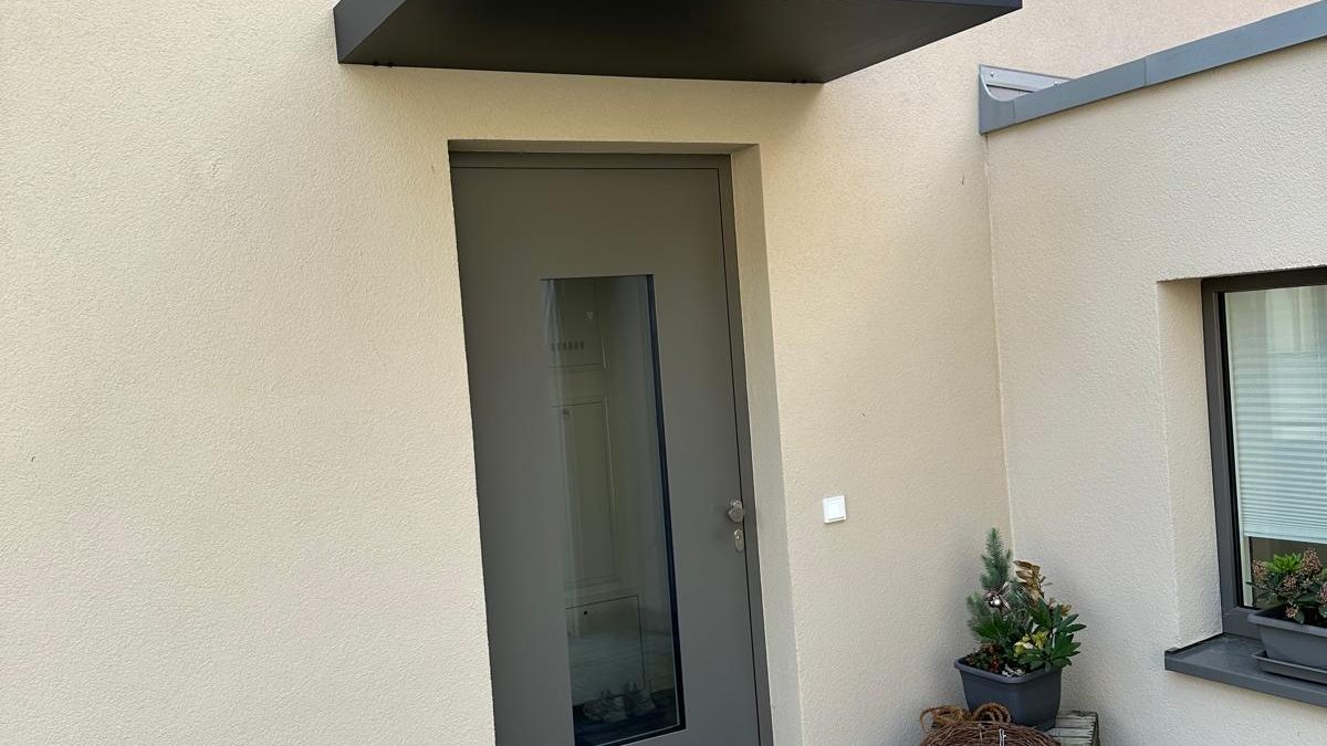 Graue Haustür mit schmalem Glasausschnitt unter einem dunklen Vordach