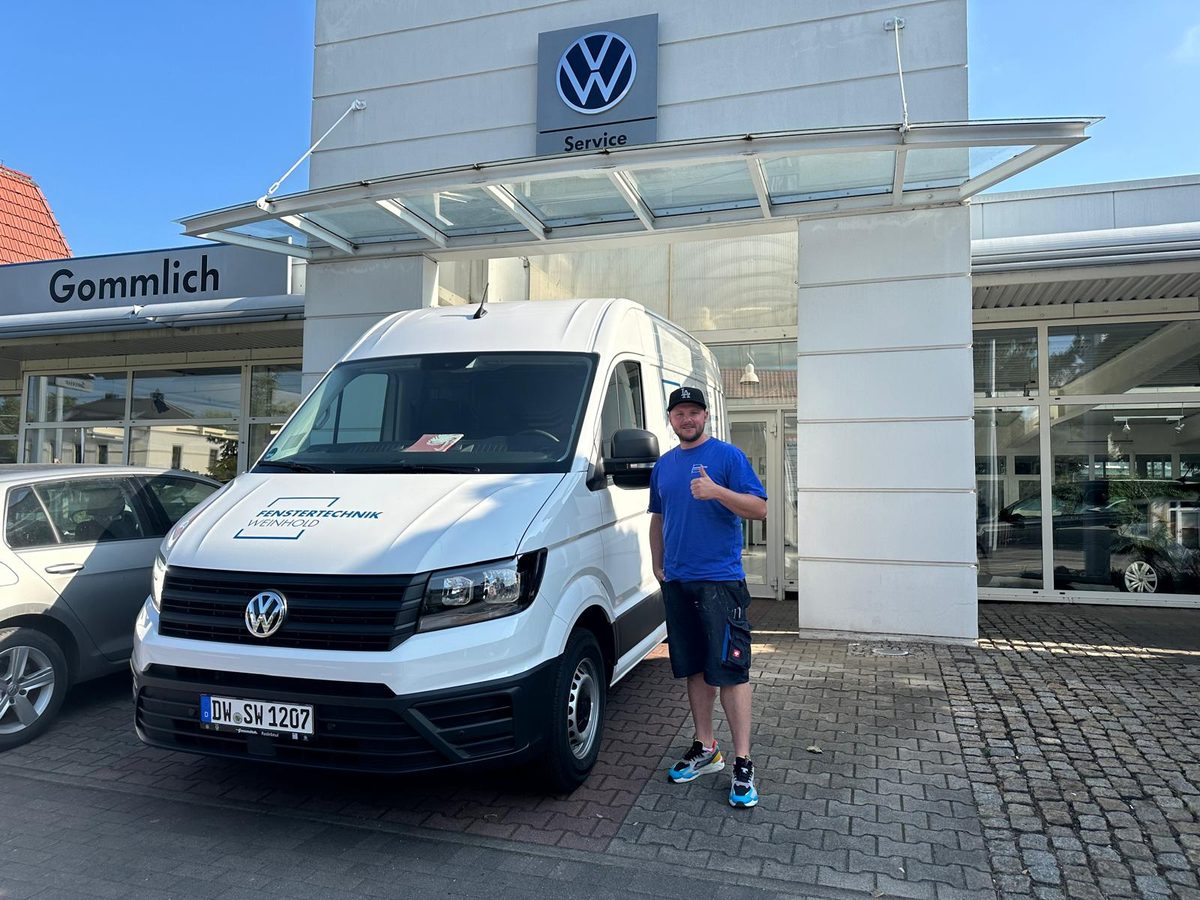 Handwerker im blauen Firmenshirt neben dem weißen Firmenwagen von Fenstertechnik Weinhold