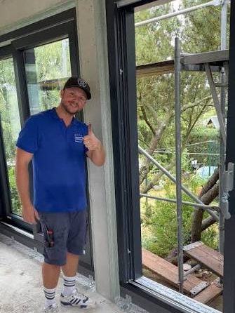 Sebastian Weinhold in blauem Firmenshirt vor neu eingebauten Fenstertüren, Daumen nach oben